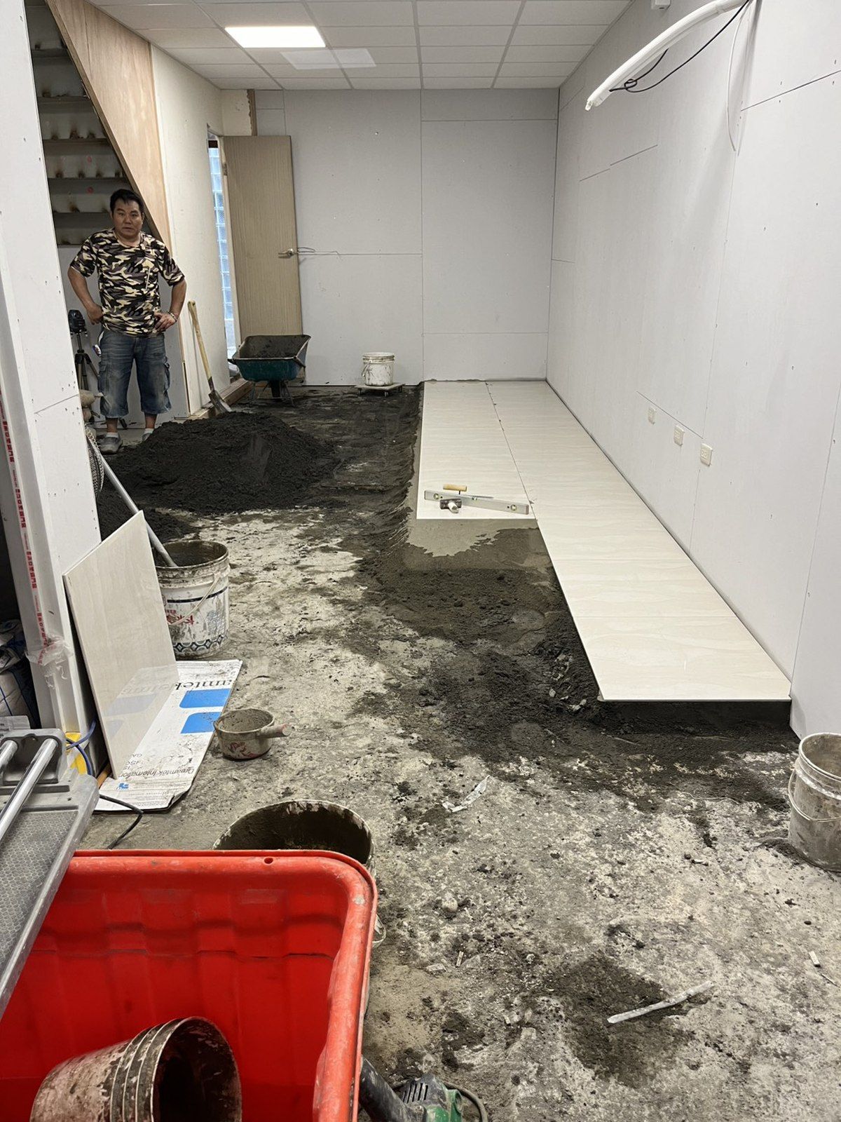 泥作施工中的地坪，砂漿鋪在地上準備抓平，右側放著待鋪的板材。